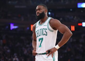 Jaylen Brown of the Boston Celtics wearing a white jersey with green trim and the number 7, hands on hips, looking intently to the left.