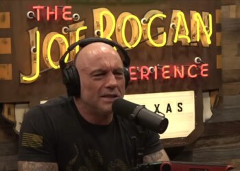 Joe Rogan wearing headphones and speaking into a microphone.