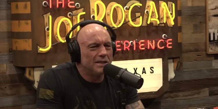 Joe Rogan wearing headphones and speaking into a microphone.