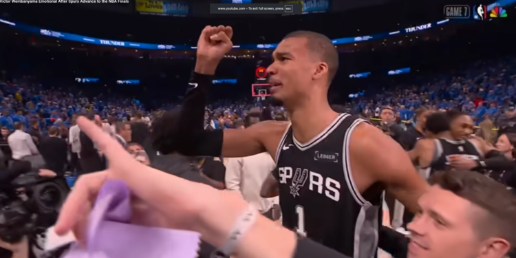 A man in a Spurs jersey raises his fist in a stadium full of people.