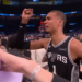 A man in a Spurs jersey raises his fist in a stadium full of people.