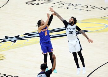 New York Knicks guard Jalen Brunson #11 hits a three-point shot over San Antonio Spurs forward Julian Champagnie #30 during the 1st half.

