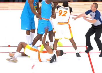 Basketball players in blue and white jerseys in an altercation, with a referee trying to intervene.