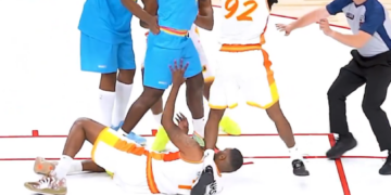 Basketball players in blue and white jerseys in an altercation, with a referee trying to intervene.
