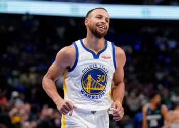 Stephen Curry smiling and wearing his Golden State Warriors jersey during a basketball game.