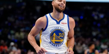 Stephen Curry smiling and wearing his Golden State Warriors jersey during a basketball game.