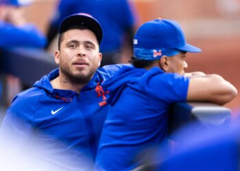 New York Mets player Francisco Alvarez in the dugout wearing a blue hoodie and cap.