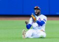 New York Mets center fielder Luis Robert Jr. sits on the ground with a look of surprise, having failed to catch a hit.