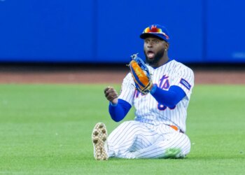 New York Mets center fielder Luis Robert Jr. sits on the ground with a look of surprise, having failed to catch a hit.