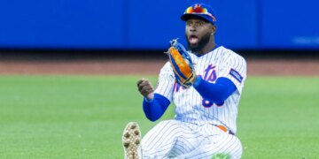 New York Mets center fielder Luis Robert Jr. sits on the ground with a look of surprise, having failed to catch a hit.