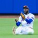 New York Mets center fielder Luis Robert Jr. sits on the ground with a look of surprise, having failed to catch a hit.