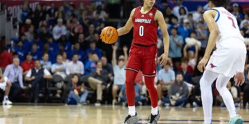 A Louisville player in a red jersey and a SMU player in a white jersey on the basketball court.