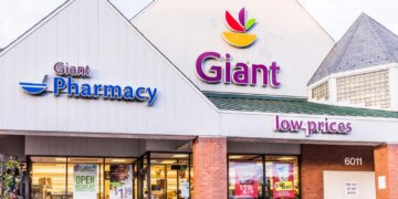 Exterior facade of a Giant grocery store and pharmacy, with "low prices" and promotional signs for ham, chicken, and shrimp visible through the windows.