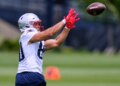 Julian Hill, wearing a white jersey and red gloves, catching a football during practice.