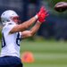 Julian Hill, wearing a white jersey and red gloves, catching a football during practice.