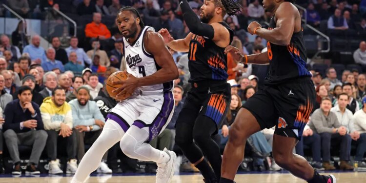 Sacramento Kings player Precious Achiuwa drives to the basket as New York Knicks players Jalen Brunson and OG Anunoby give chase.