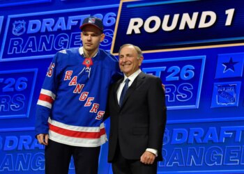 Alberts Smits, left, wearing a blue New York Rangers jersey, stands with NHL Commissioner Gary Bettman, right, at the NHL draft.