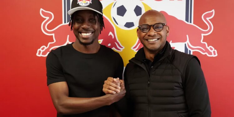 Two men, one in a Red Bull cap, shake hands and smile in front of a Red Bull logo.