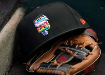 A black San Francisco Giants baseball cap with a rainbow "SF" logo rests on a baseball glove.