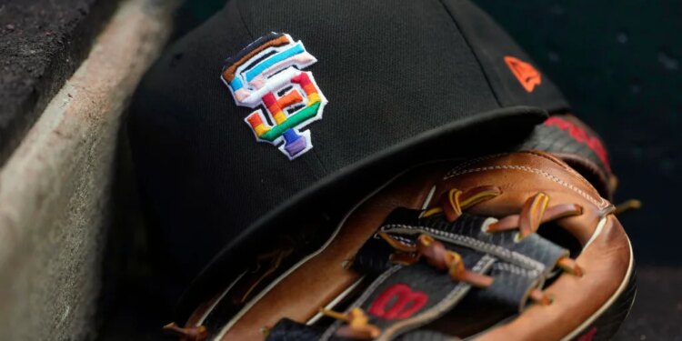 A black San Francisco Giants baseball cap with a rainbow "SF" logo rests on a baseball glove.
