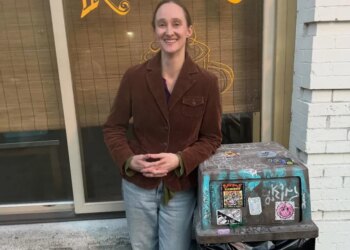 Seattle Mayor Katie Wilson laughs next to a trash can with a business displaying "KATY'S" in the background.