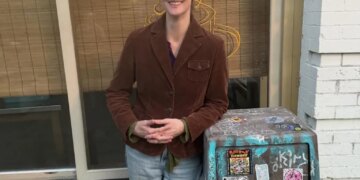 Seattle Mayor Katie Wilson laughs next to a trash can with a business displaying "KATY'S" in the background.