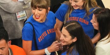 Taylor Swift, in a blue shirt, speaks and smiles at an event.