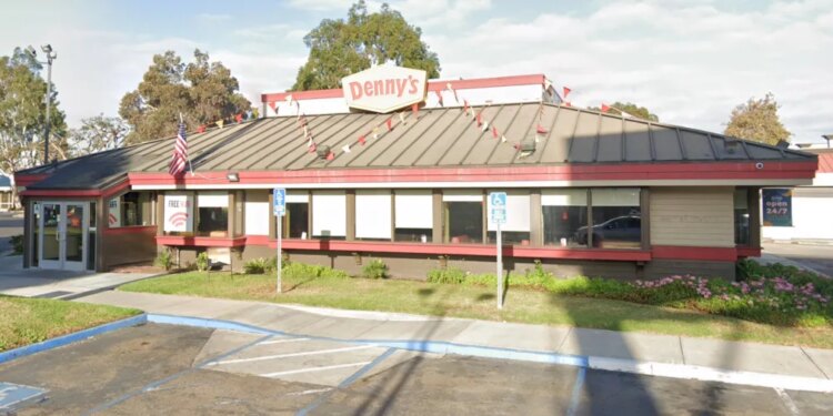 Exterior view of a Denny's restaurant with a red and white sign on the roof, an American flag, and "Open 24/7" banner.