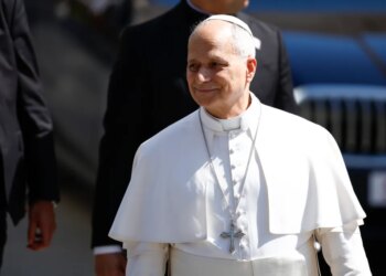 Pope Leo XIV smiling, wearing white papal attire and a silver crucifix.