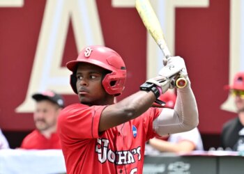 A baseball player in a red helmet and "St. John's" jersey holding a bat.