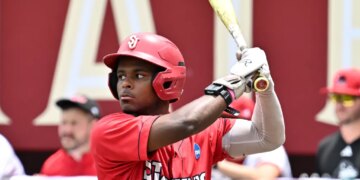 A baseball player in a red helmet and "St. John's" jersey holding a bat.
