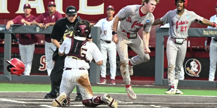 A St. John's baseball player in a gray striped uniform leaps over a Florida State catcher.