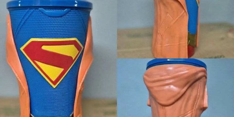 A Supergirl movie drink cup with a blue cup, Superman logo, gold belt buckle, and orange jacket.