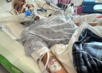 A young Spurs fan in a hospital bed with medical equipment, including a neck brace and an IV in his arm.