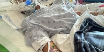 A young Spurs fan in a hospital bed with medical equipment, including a neck brace and an IV in his arm.