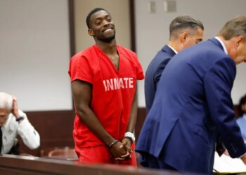 Terrion Arnold in red inmate uniform and handcuffs, smiling in court.