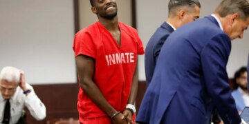 Terrion Arnold in red inmate uniform and handcuffs, smiling in court.