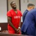 Terrion Arnold in red inmate uniform and handcuffs, smiling in court.