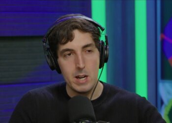 A man wearing headphones and a black shirt speaking into a microphone, with colorful digital art in the background.