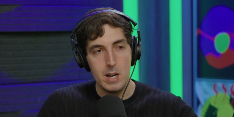 A man wearing headphones and a black shirt speaking into a microphone, with colorful digital art in the background.