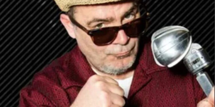 Trevor Carey, wearing a straw fedora and sunglasses, holding a vintage microphone and making a fist.