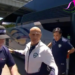 A bald man wearing a white and navy jacket with a UFA logo walking past a security guard and a bus.