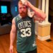 A man with a bloodied face and arm, wearing a green Celtics jersey, holds a white towel to his head.