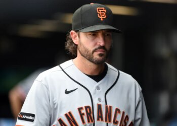 A San Francisco Giants player in a grey jersey and black cap looks off to his right.