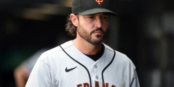 A San Francisco Giants player in a grey jersey and black cap looks off to his right.
