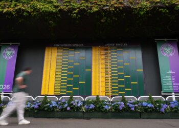 A visitor walks by the Gentlemen's Singles and Ladies' Singles match boards at Wimbledon.