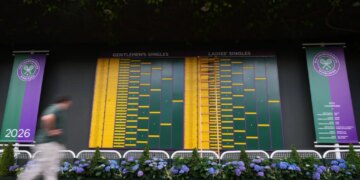 A visitor walks by the Gentlemen's Singles and Ladies' Singles match boards at Wimbledon.