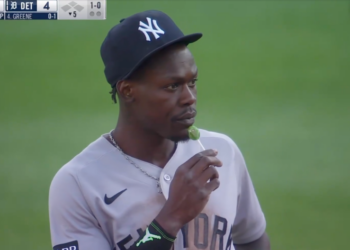Baseball player in a New York Yankees uniform and cap eating a green lollipop.