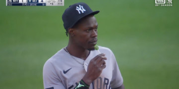 Baseball player in a New York Yankees uniform and cap eating a green lollipop.