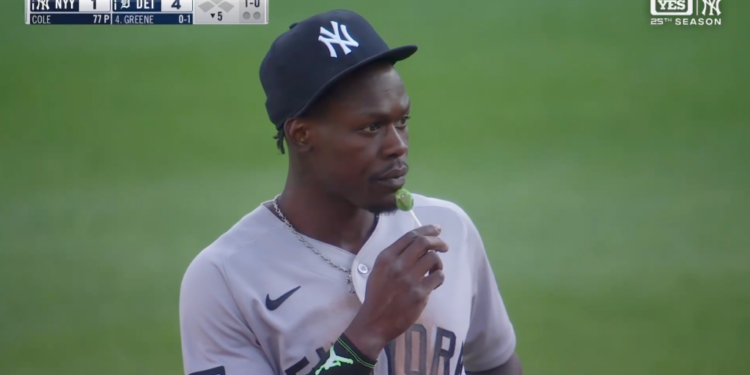 Baseball player in a New York Yankees uniform and cap eating a green lollipop.